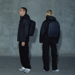 A man and woman standing wearing an Everyday Backpack in Midnight Blue on their backs