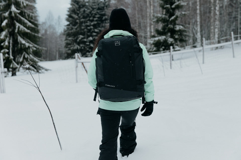 A women walking through the know wearing a green jacket and black backpack
