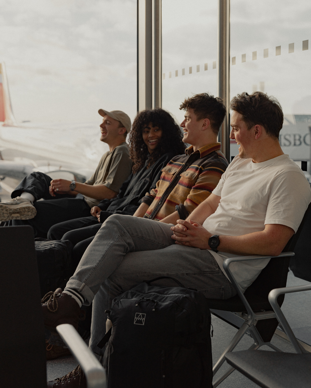 Friends waiting in an airport, with a black Stubble & Co bag resting by one person's feet.
