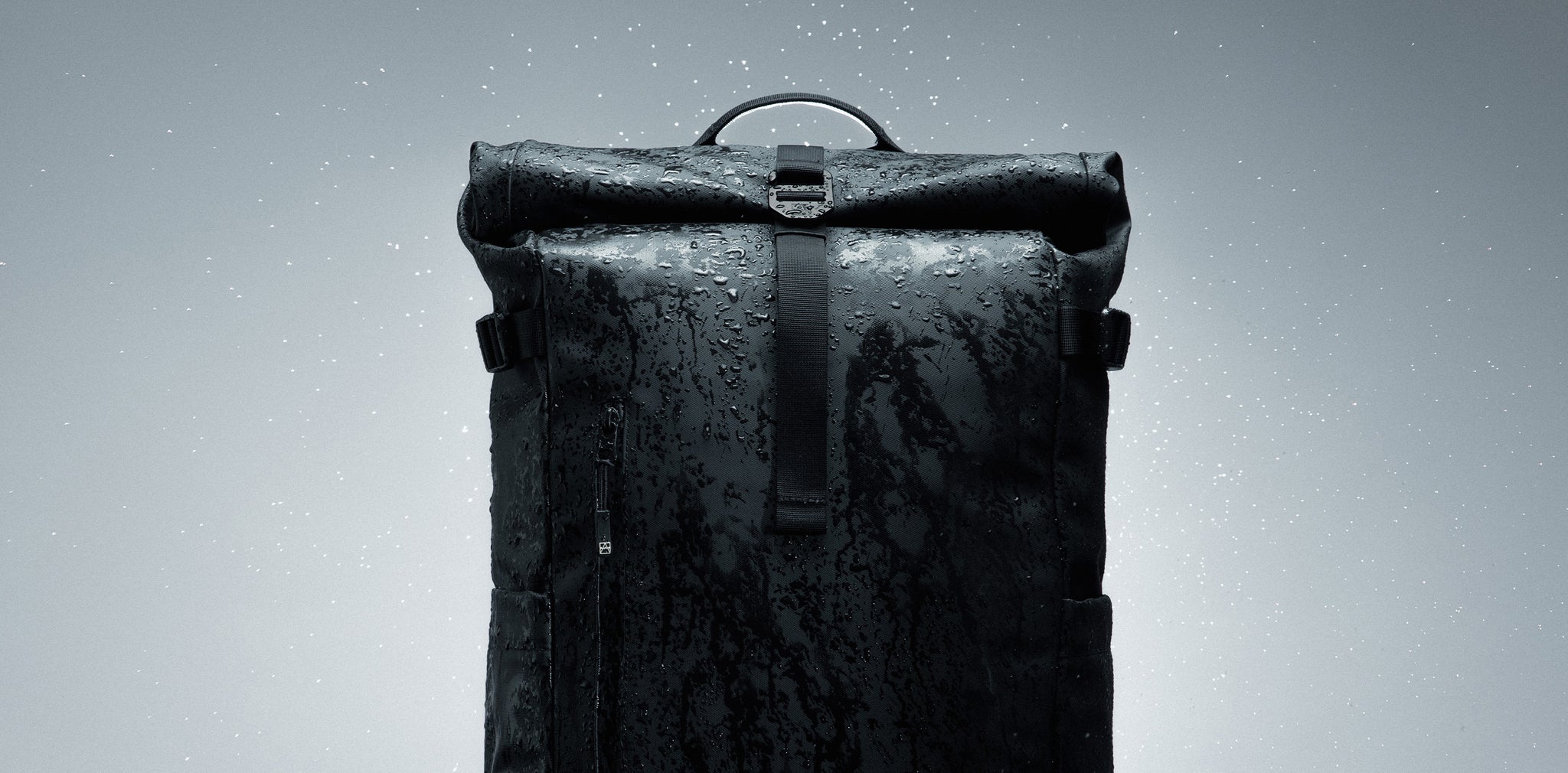 Black Roll Top backpack on a gray background with water beads on the fabric 