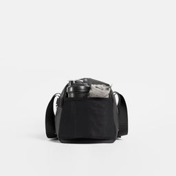 A studio shot of the end mesh pocket with a bottle and towel inside on the Gym Duffel 25L in All Black