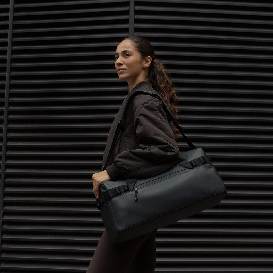 A woman wearing a gym duffel 25l in All Black on her shoulder