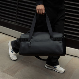 A close up of the gym duffel 25l in All Black being carried at a mans side
