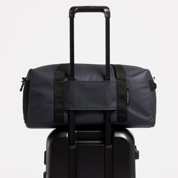 A studio shot of the Midnight Blue Gym Duffel on a suitcase using a trolley sleeve