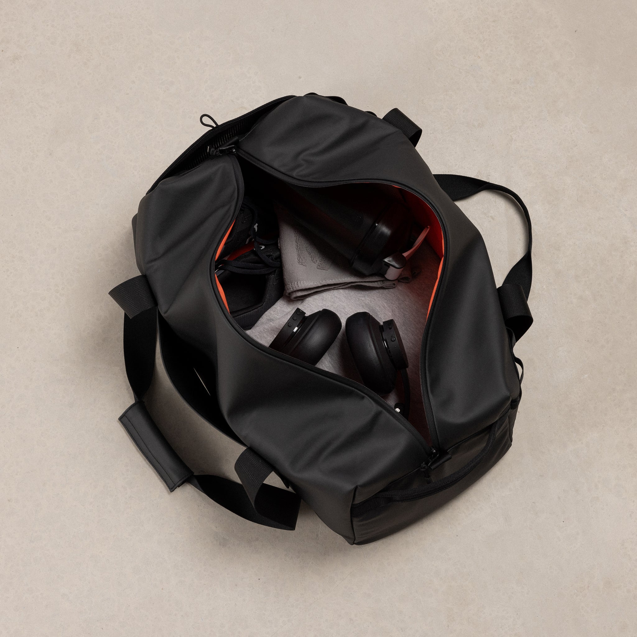 A studio shot of the gym duffel 25l in All Black with gym accessories inside including trainers, headphones, water bottle and shaker