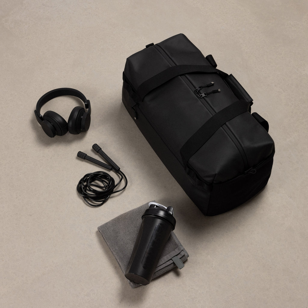 A studio shot of the gym duffel 25l in black with the content around including a skipping rope, headphones and towel