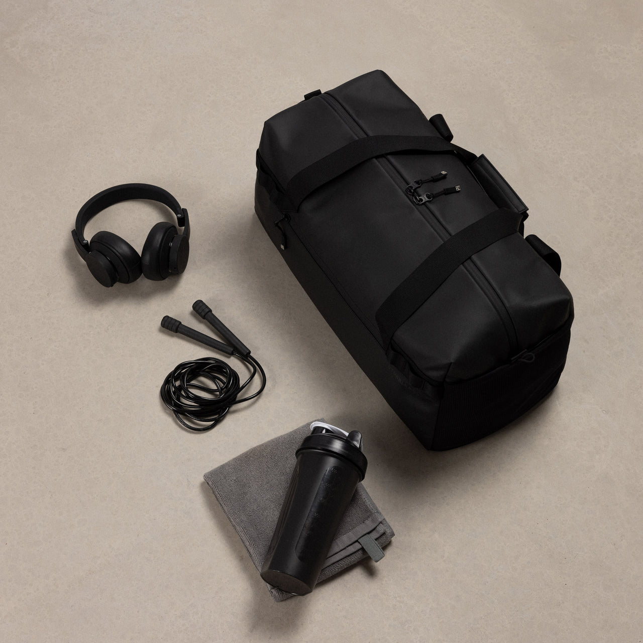 A studio shot of the gym duffel 25l in All Black with the content around including a skipping rope, headphones and towel