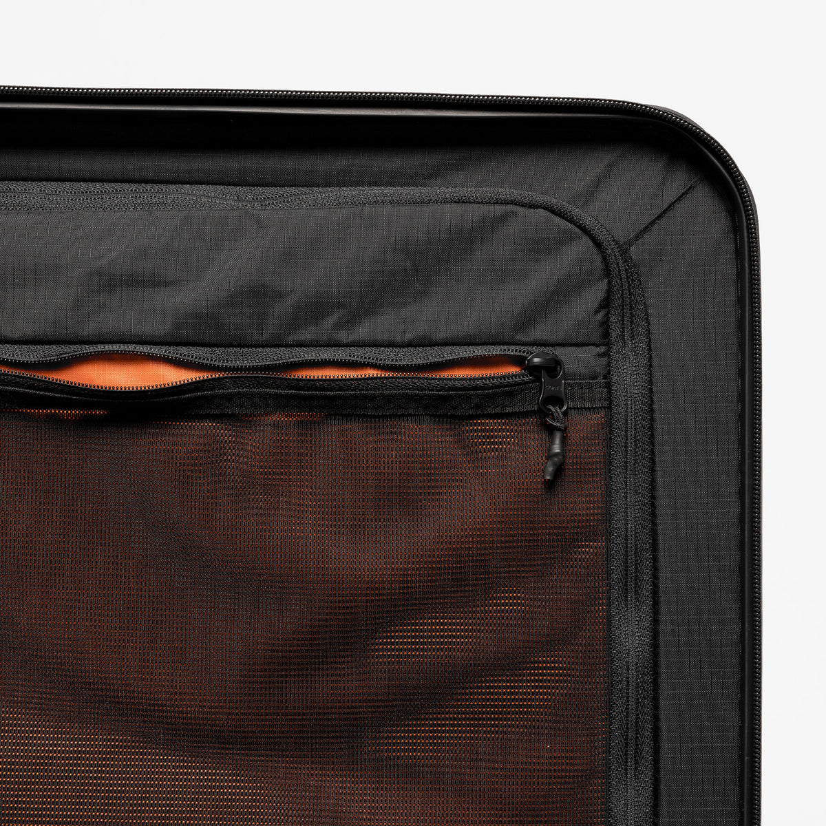 Close-up of a black suitcase or luggage compartment showing a mesh interior pocket with an orange lining and a zipper.