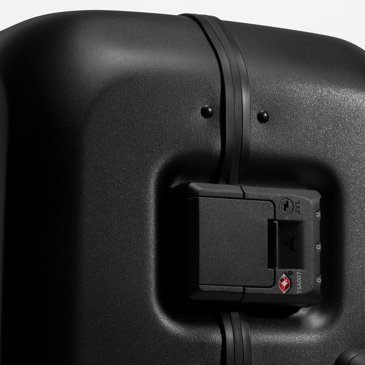 Close-up of a black hard-shell suitcase showing the tsa lock compartment and zipper area against a light gray background.