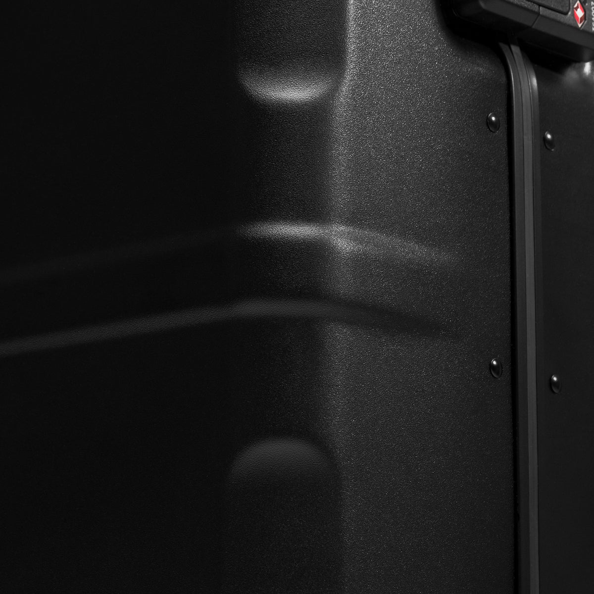 Close-up detail of a black hard-sided suitcase, showing textured plastic shell, rivets, and part of a lock mechanism.