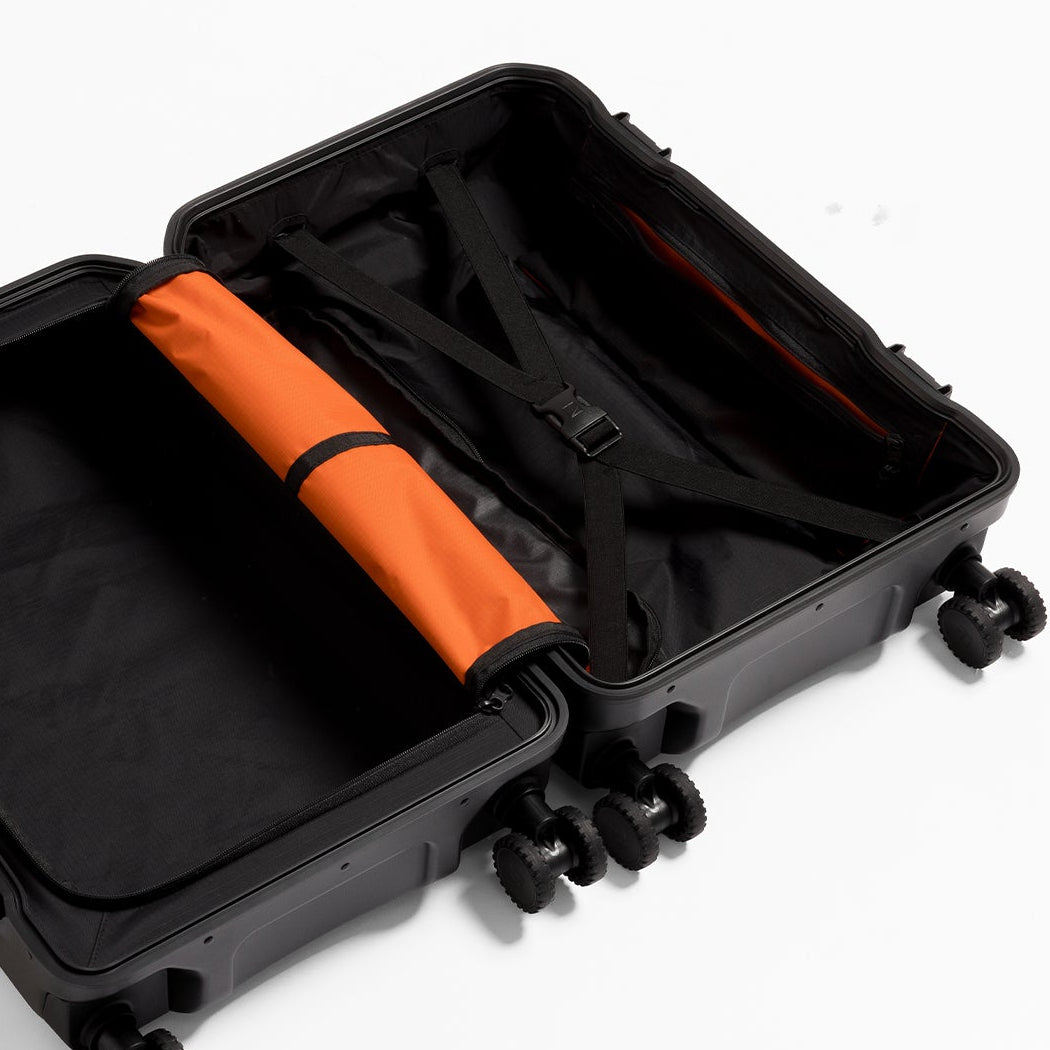 An open black hard-shell suitcase with four wheels, showing a black interior lining and a rolled orange divider, photographed on a clean white background.