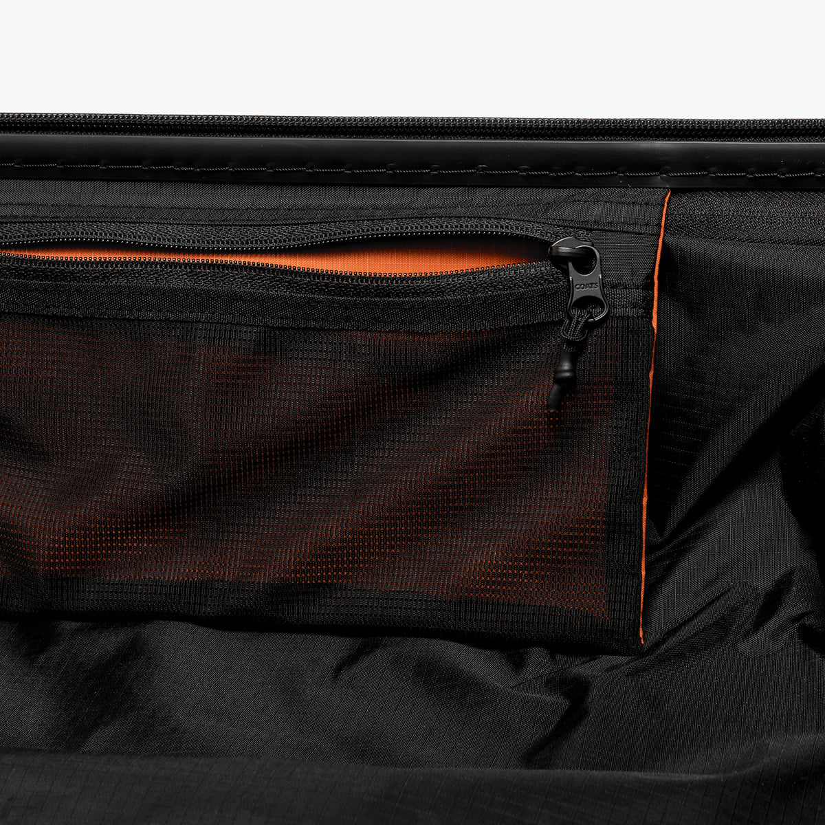 Close-up of a black mesh zippered pocket with orange lining and orange contrast stitching on a black bag.