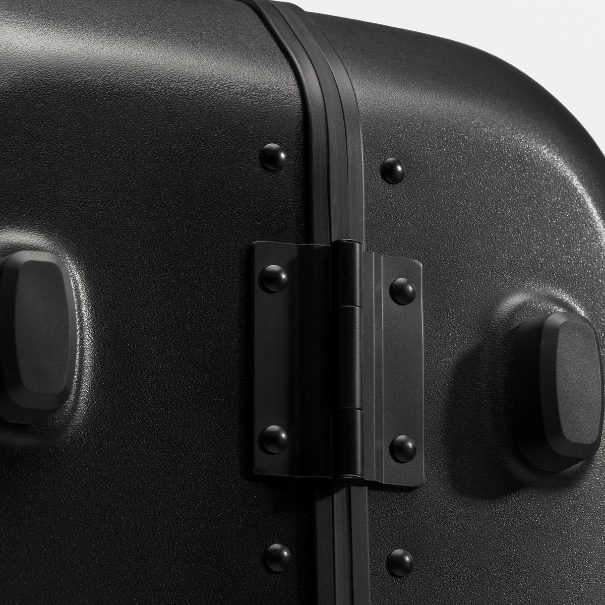Close-up of a black hard-shell suitcase showing the hinge, rivets, and padded feet.