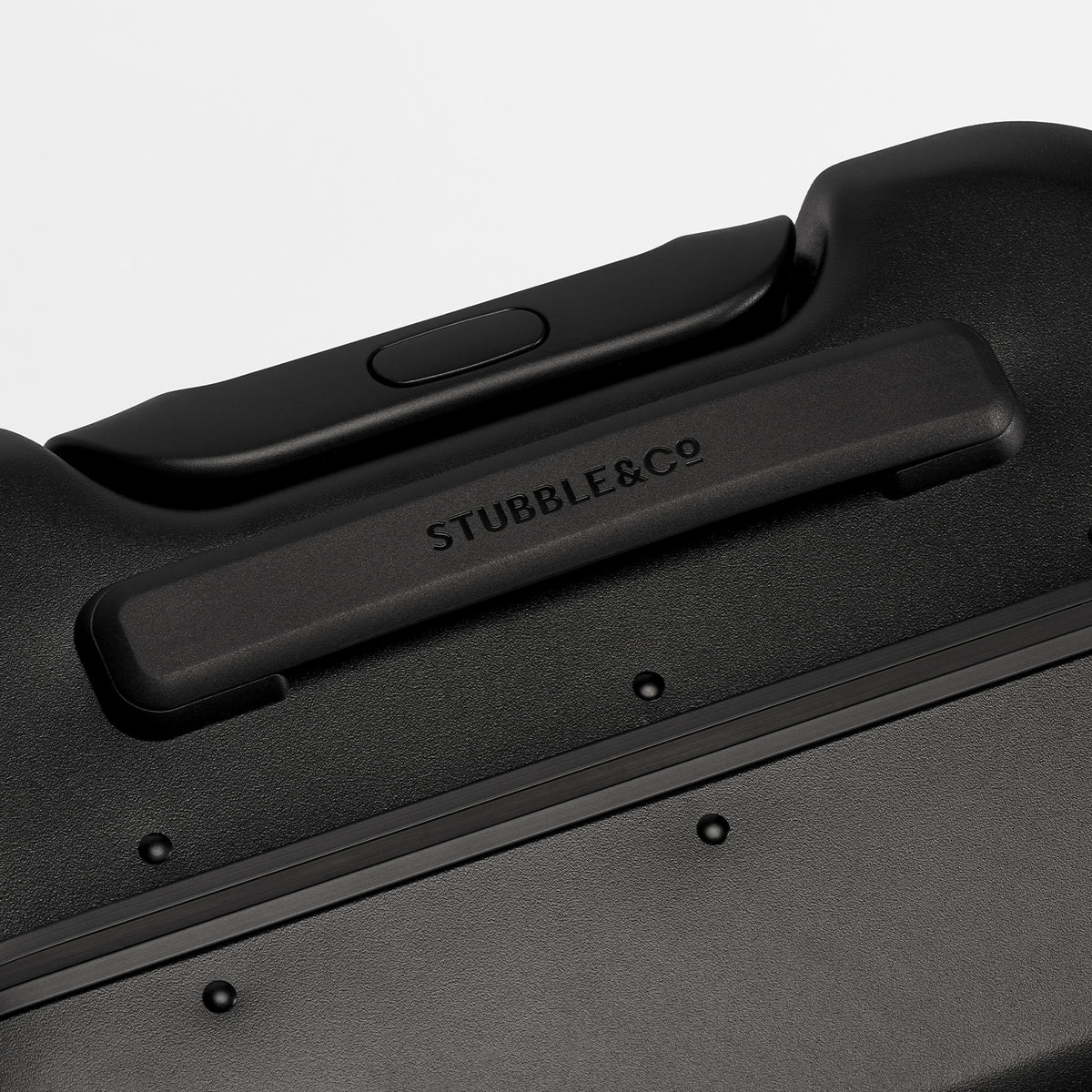 Close-up of a black hard-shell suitcase showing the handle attachment area with the debossed brand name STUBBLE&Co.