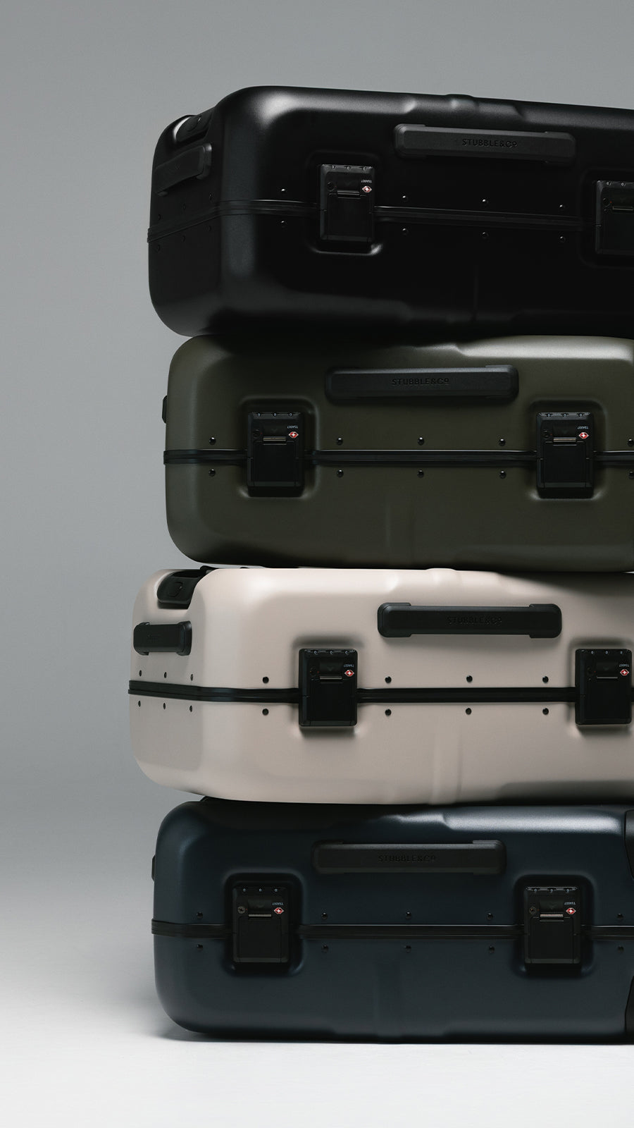 Four hard-shell carry-on suitcases stacked vertically on a light gray studio background. From top to bottom, the colors are black, olive green, off-white/cream, and dark navy blue.