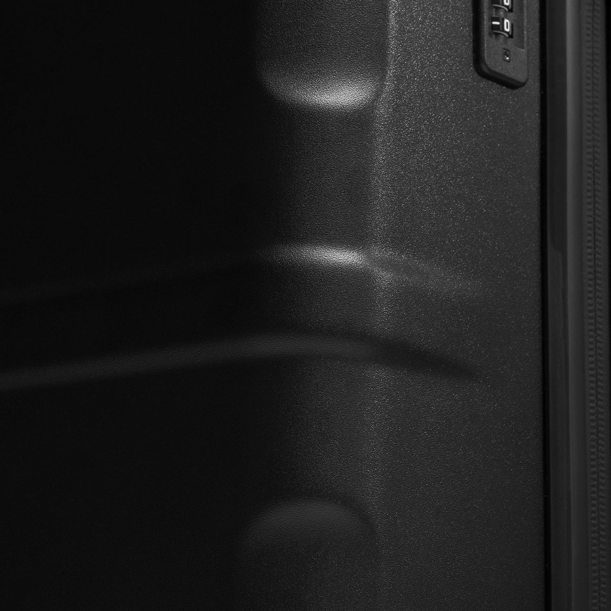 Close-up detail of a black suitcase with a zipper and part of a combination lock.