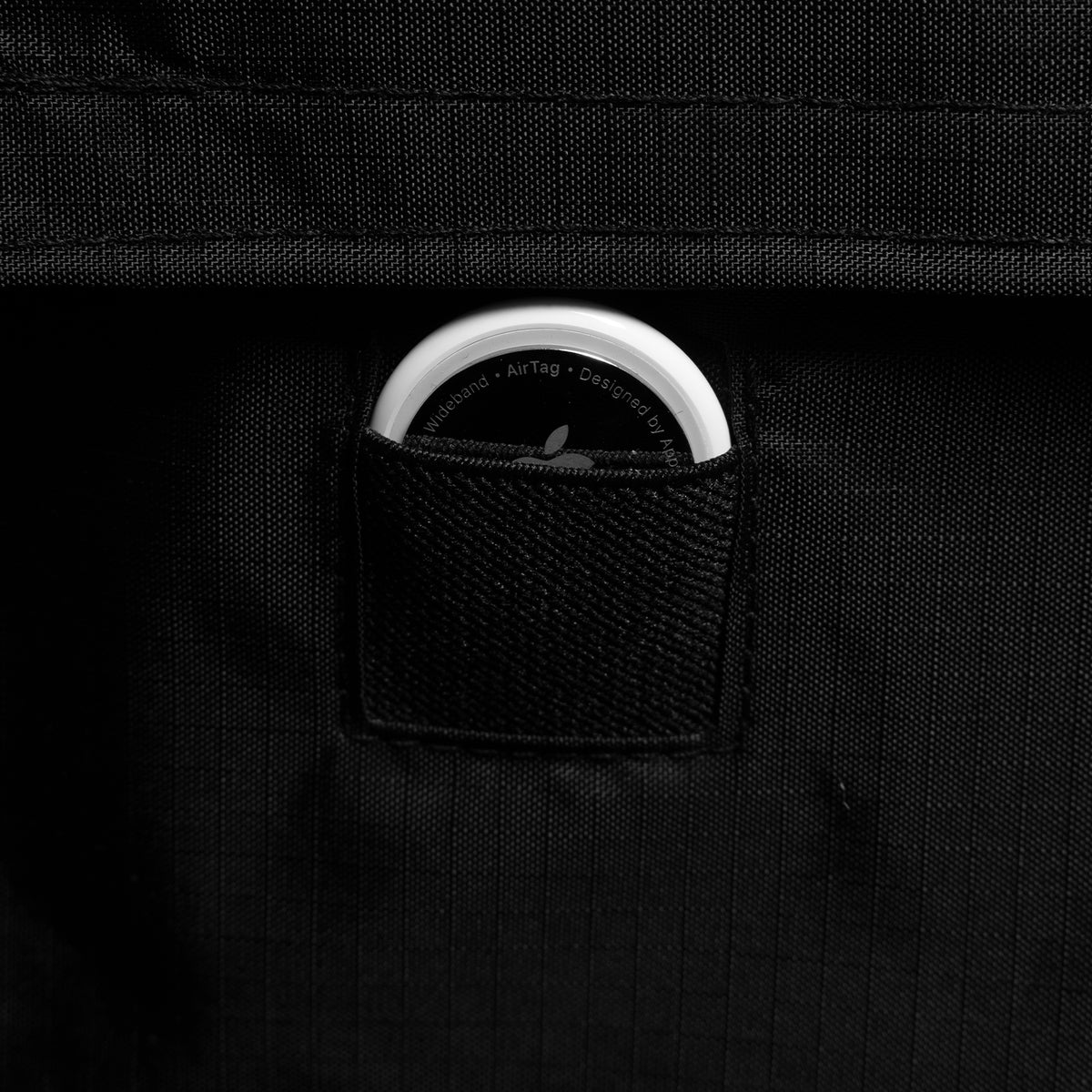 A close-up of a black fabric pouch holding a white circular AirTag.