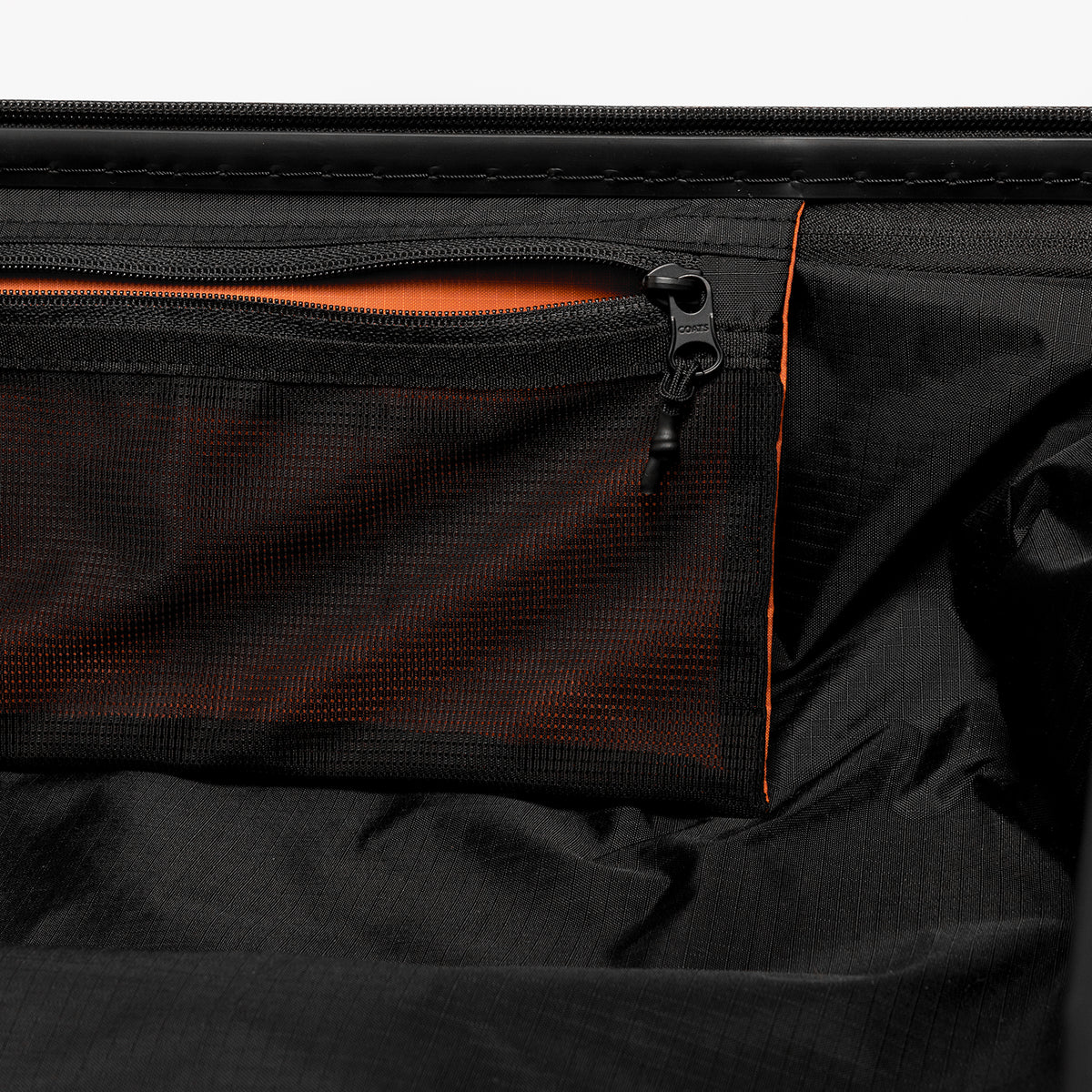 Close-up of a black zippered compartment with a mesh pocket and bright orange contrast stitching and lining.