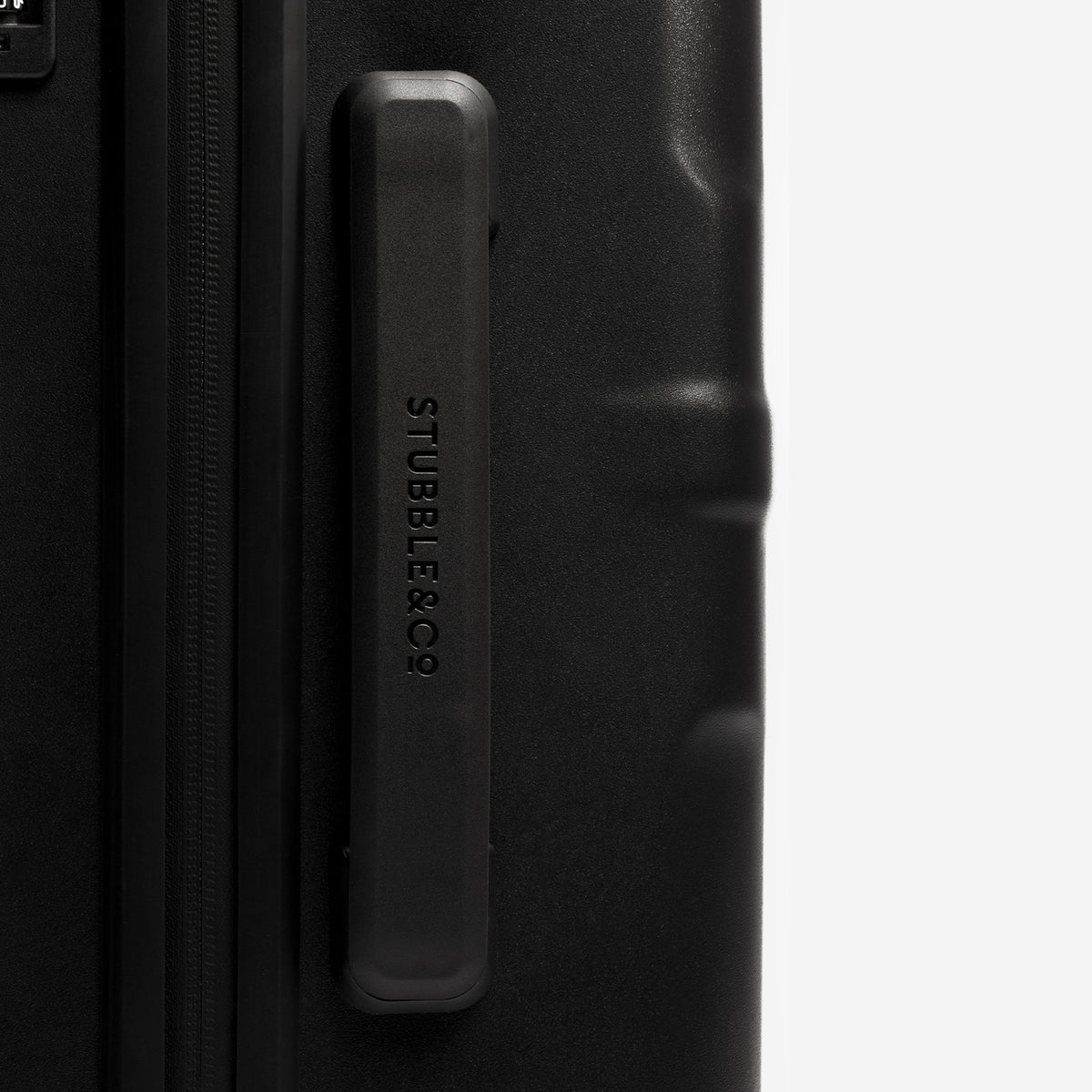 Close-up of a black hard-shell suitcase showing a textured side handle with the brand name 'STUBBLECO' embossed vertically, set against a plain light gray background.