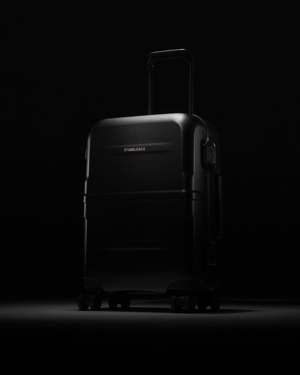 Hardshell suitcase standing upright with its handle extended, lit against a black studio background.