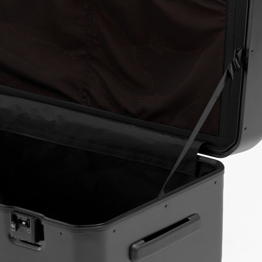 A black hard-shell suitcase shown open, revealing a dark brown interior lining and zippered compartments, photographed on a clean white background.
