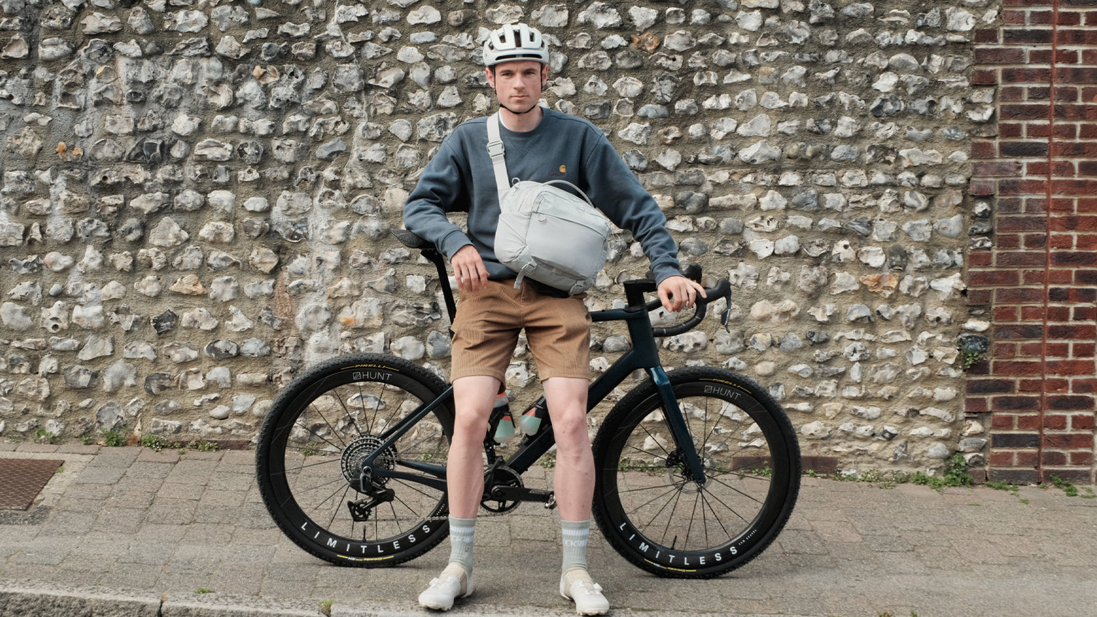Man leaning on a bike with Hunt wheels, wearing the Motion Sling 15L in Ash. 
