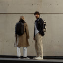 A man and woman wearing Hybrid Backpack 20L in sand and All Black on their backs