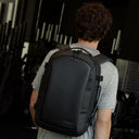 A man walking through a gym with a Hybrid Backpack 20L in All Black on his back