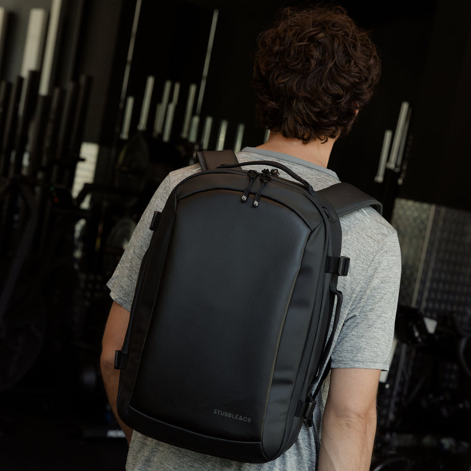 A man walking through a gym with a Hybrid Backpack 20L in All Black on his back