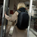 A woman entering a building wearing a Hybrid Backpack 20L in All Black on her back