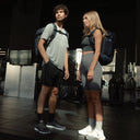 A studio shot of a man and woman standing in a gym with Hybrid Backpack 20L in Midnight Blue on their backs