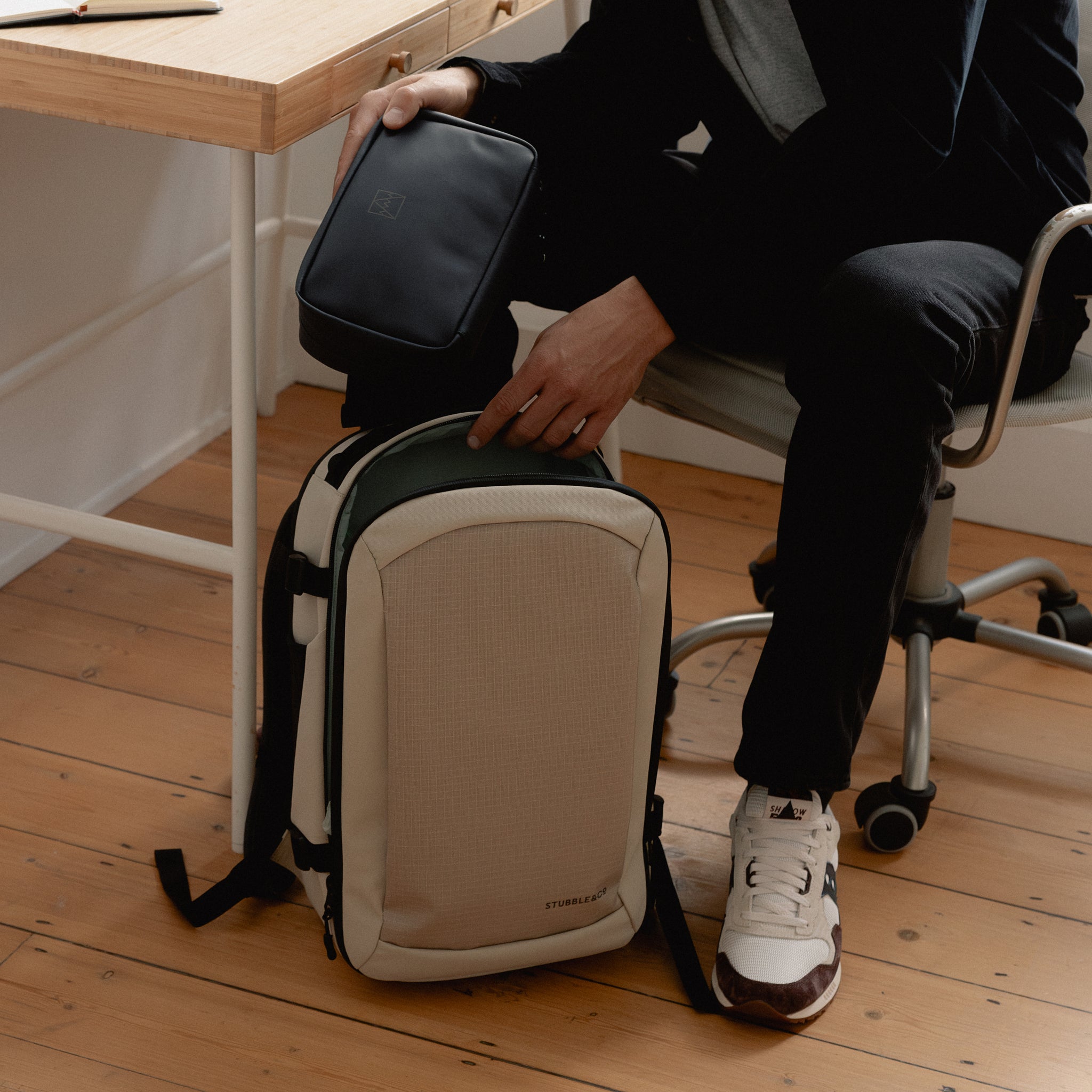 A man placing a tech bag into a Hybrid Backpack 20L in Sand