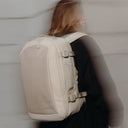 A woman wearing the Tonal Sand Hybrid Backpack 20L on her back with a blurred affect but the back in focus