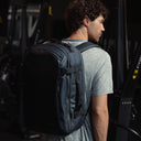 A man standing in a gym wearing a Midnight Blue Hybrid Backpack 30L on her back