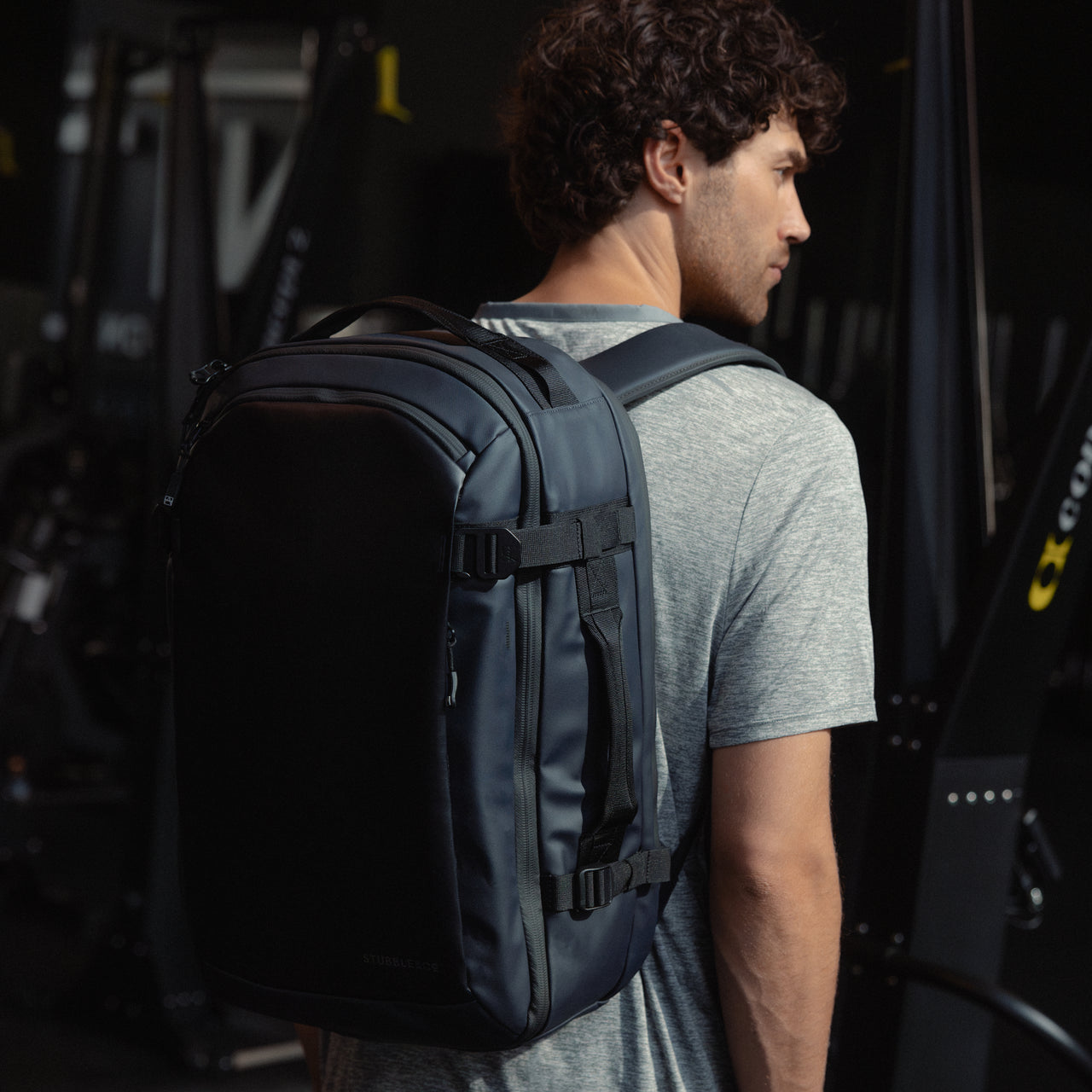 A man standing in a gym wearing a Midnight Blue Hybrid Backpack 30L on her back