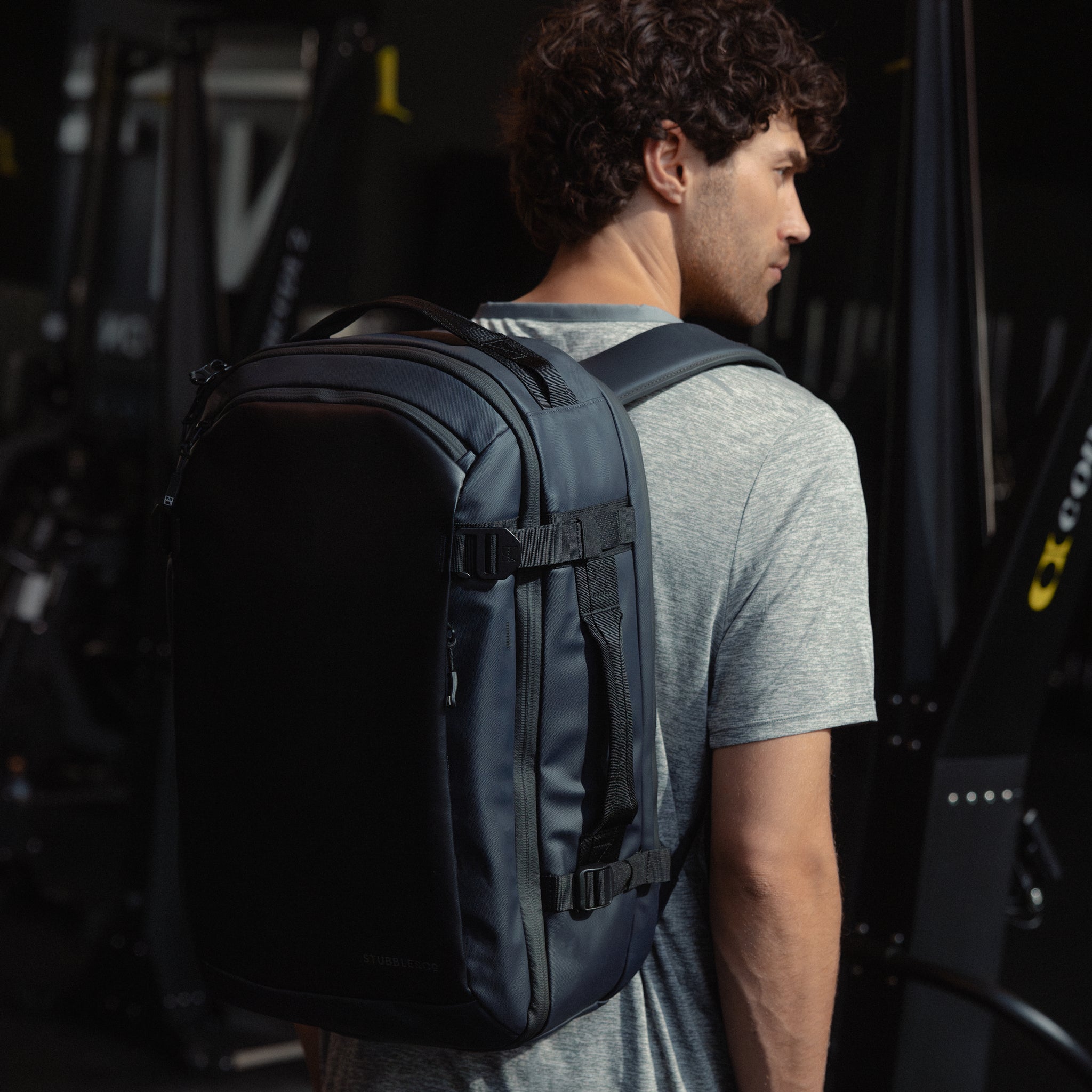A man standing in a gym wearing a Midnight Blue Hybrid Backpack 30L on her back