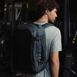 A man standing in a gym wearing a Midnight Blue Hybrid Backpack 30L on her back