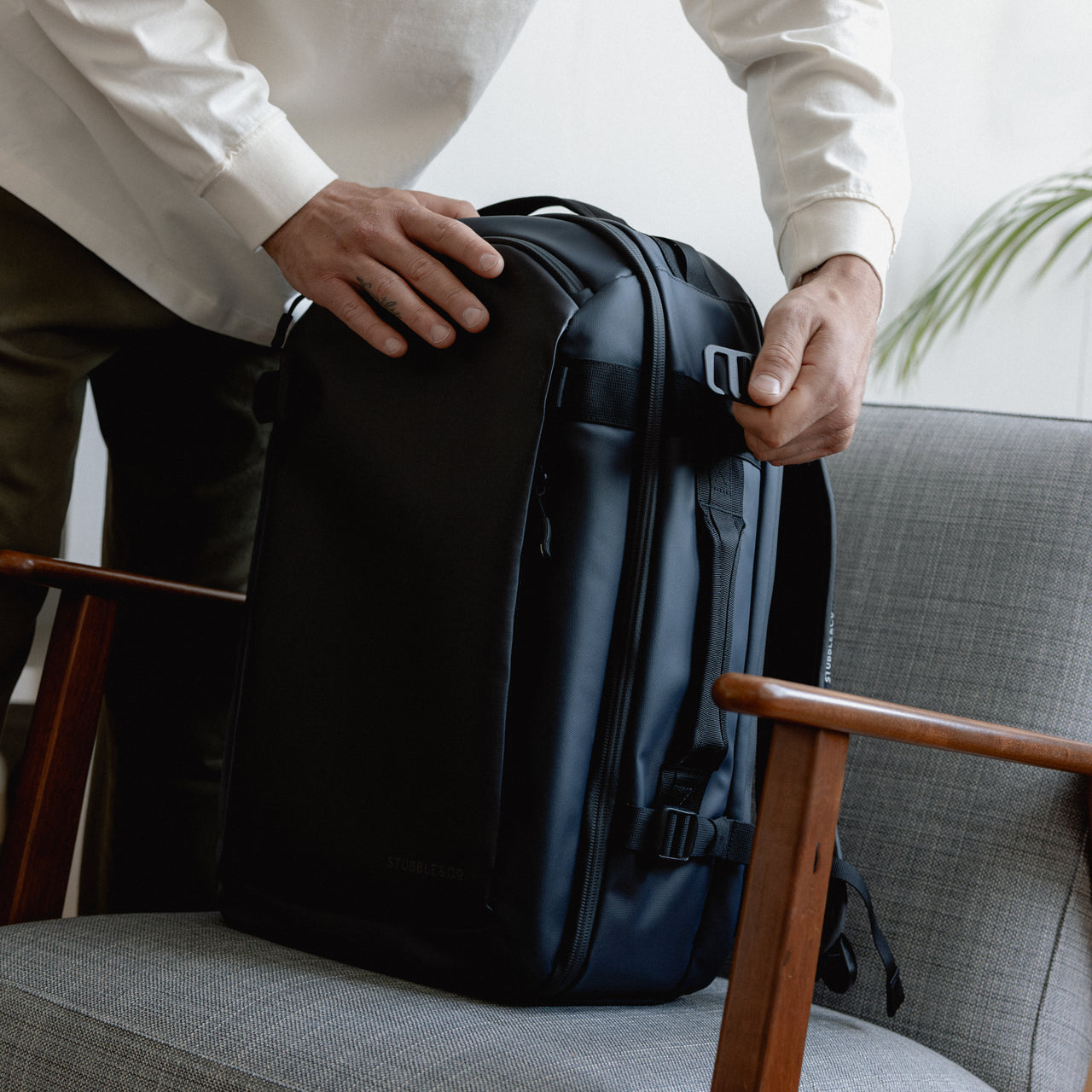 A man doing up the g-hook compression strap on the side of a Midnight Blue Hybrid Backpack 30L