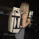 A woman standing side on wearing a Hybrid Backpack 30L in Sand on her back