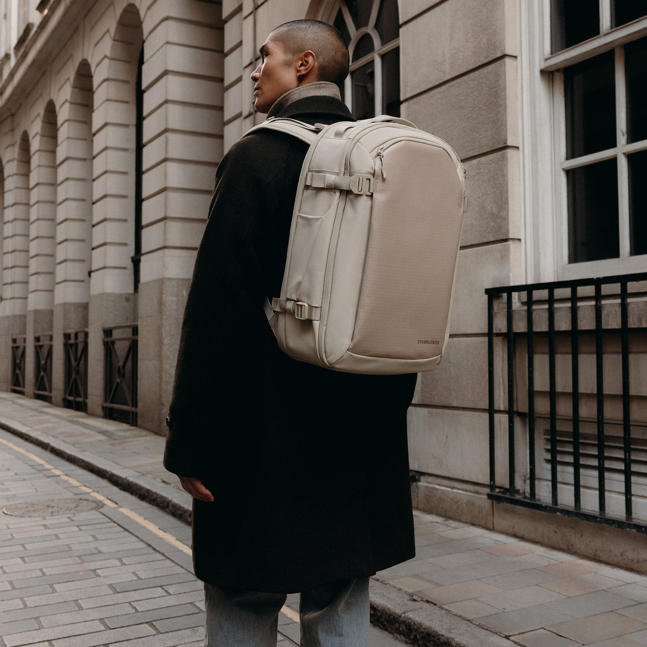 A man walking down a street with a Hybrid Backpack 30L in Tonal Sand on his back