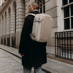A man walking down a street with a Hybrid Backpack 30L in Tonal Sand on his back