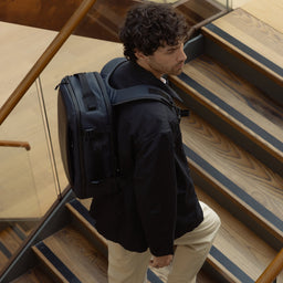 A man walking up some stairs wearing a Midnight Blue Hybrid Backpack 20L on his  back