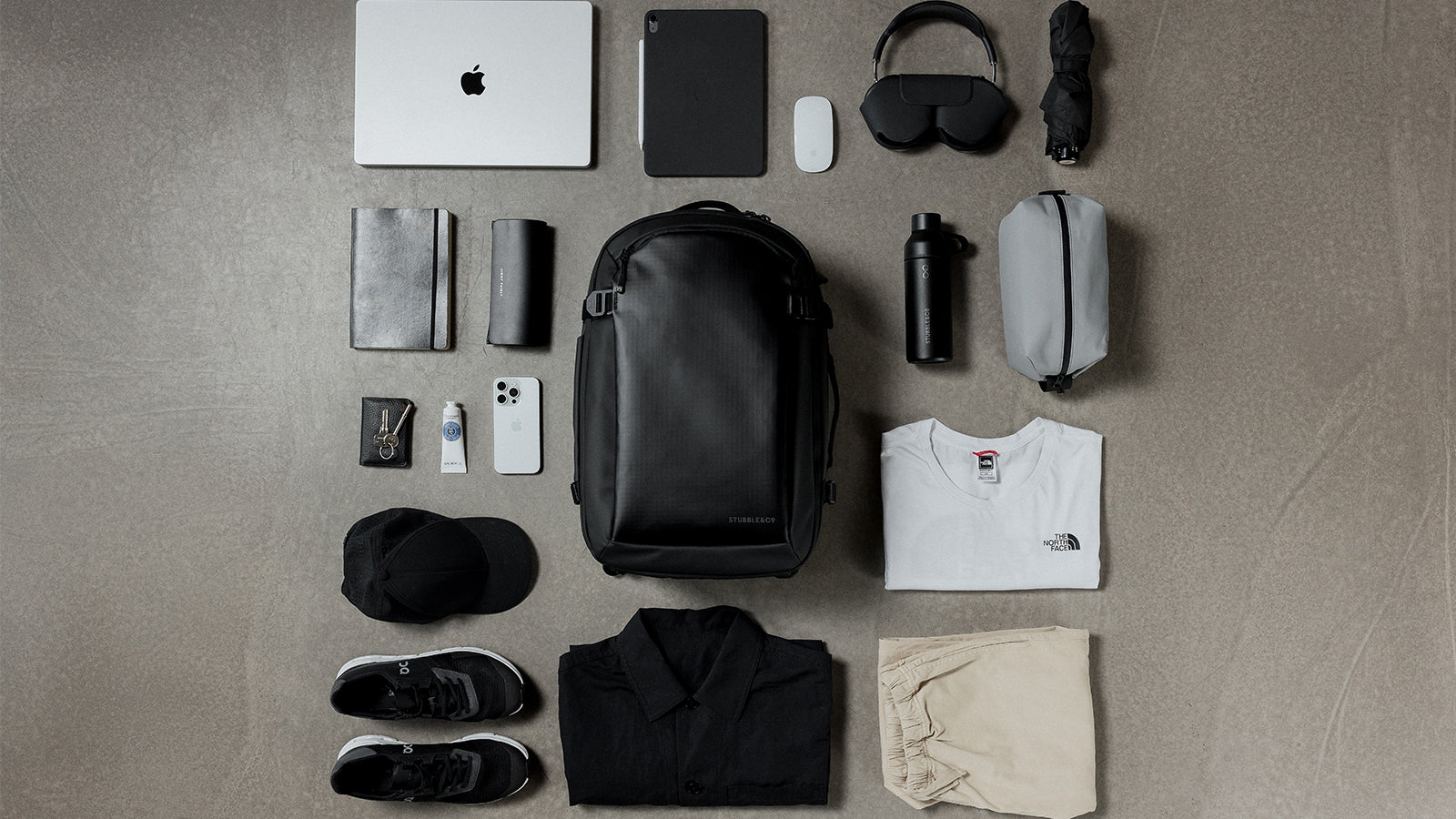 The hybrid backpack 30L in black on the floor of the studio surrounded by folded clothes ready for packing