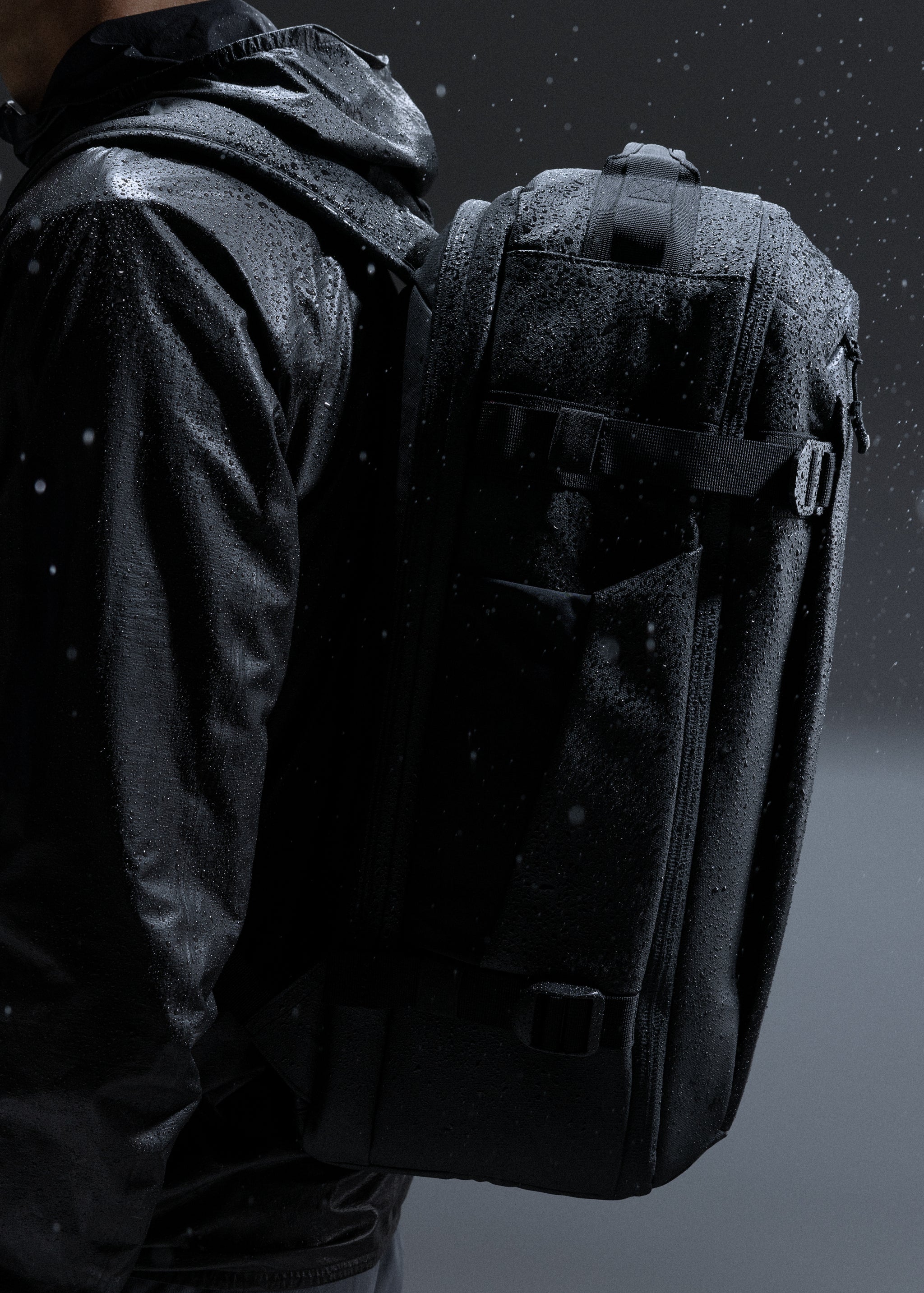 A man wearing a Hybrid Backpack 30L on his back whilst water is sprayed showing the waterproof materials