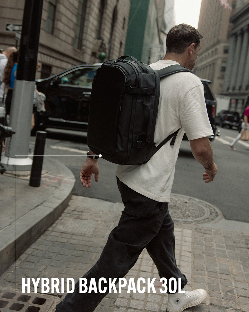 A man wearing a hybrid backpack 30l on his back as he crosses the street with product name annotated
