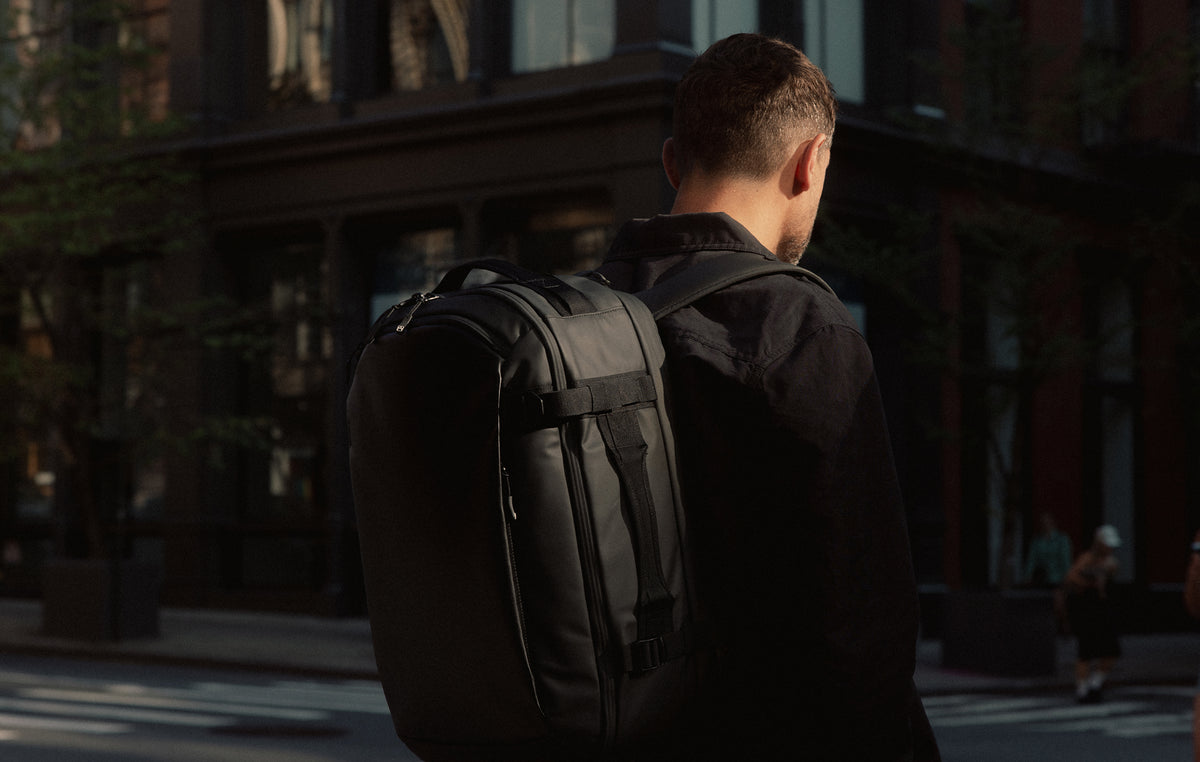 male wearing a black backpack in a city street with sunlight on this face