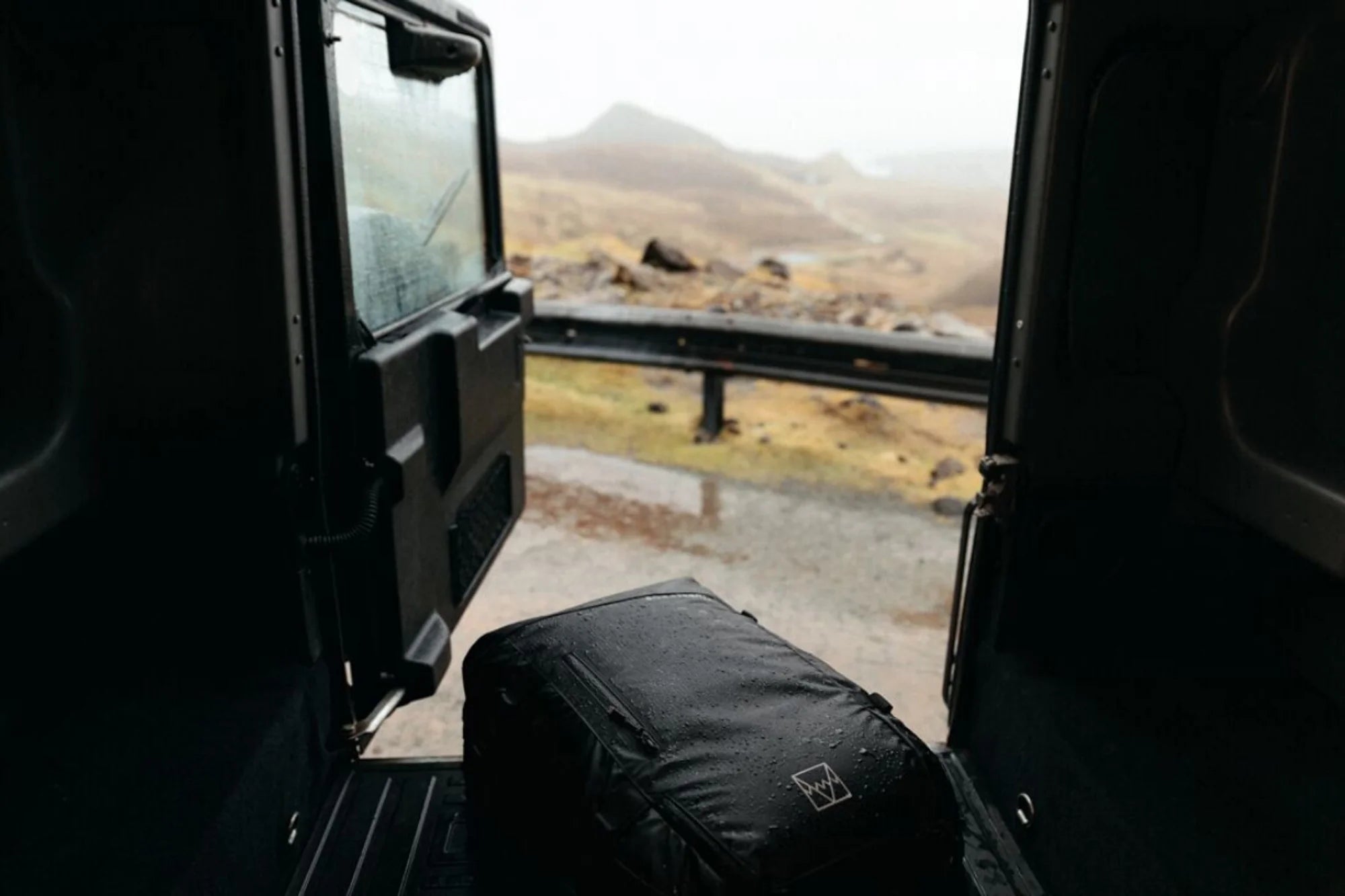 A black Adventure bag in black in the back of a defender in the Scottish highlands