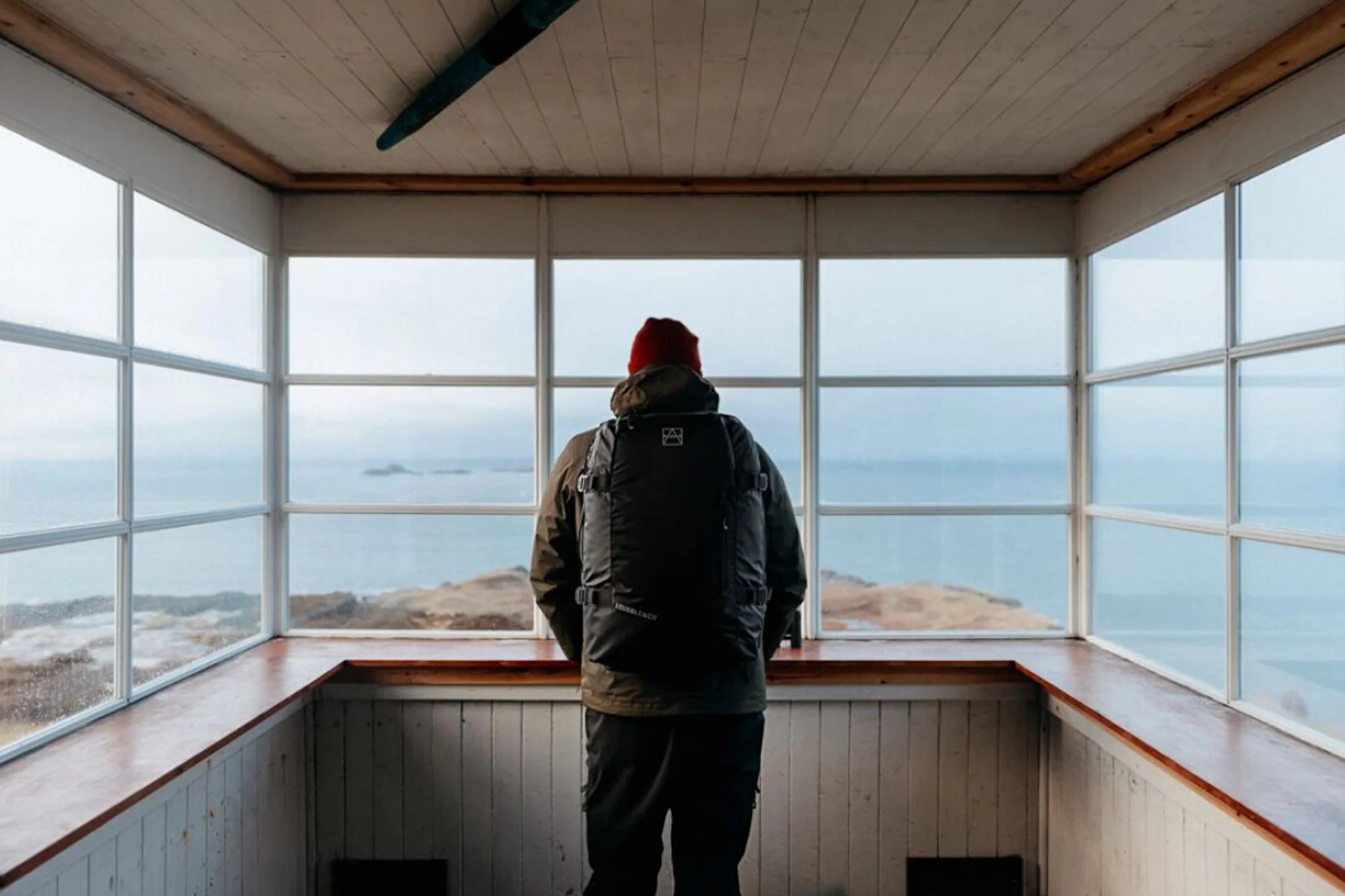 A man standing in a view point by the coast with an Adventure Bag in black on his back