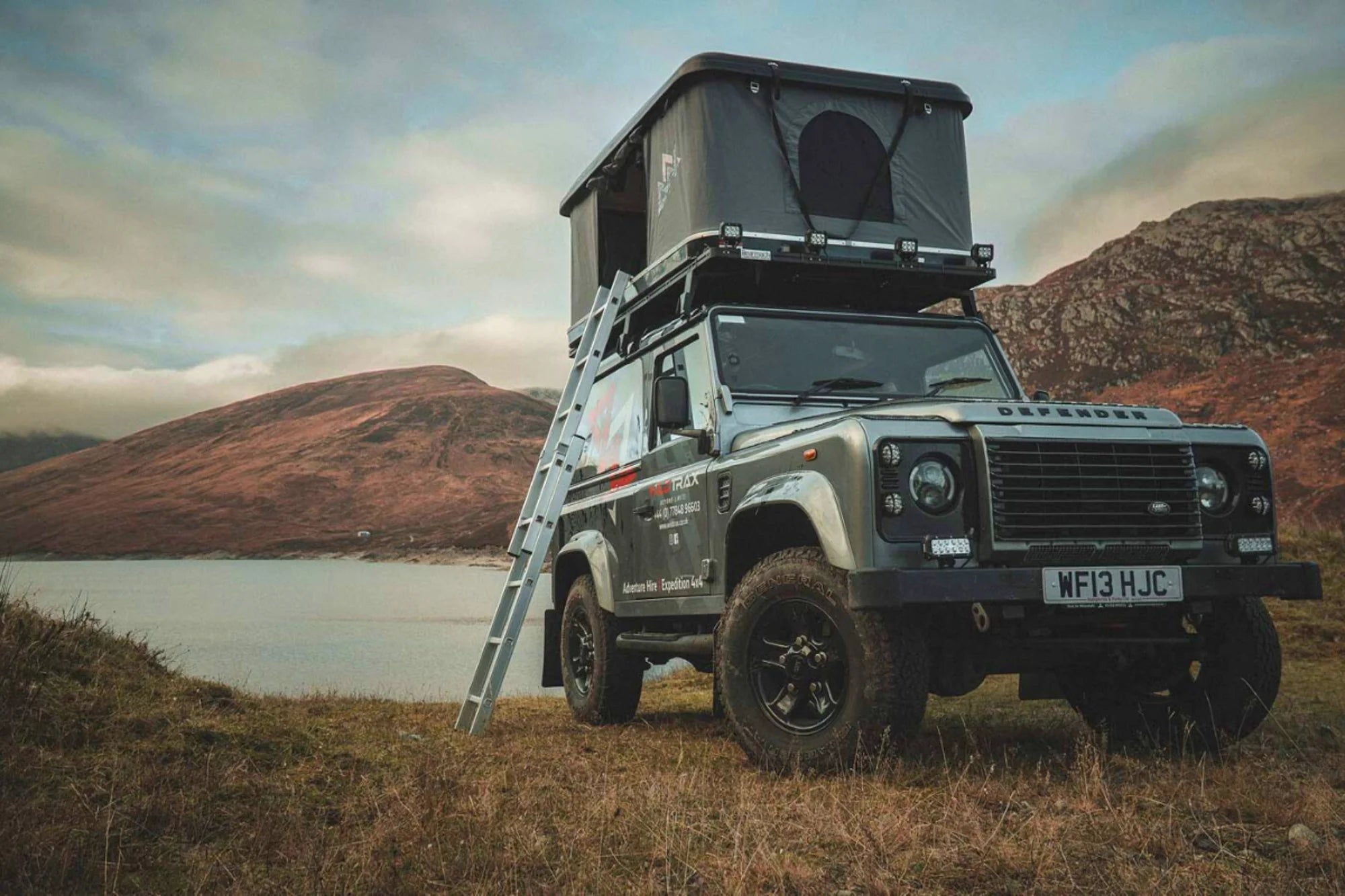 A land rover defender by a lake with a tent box on top