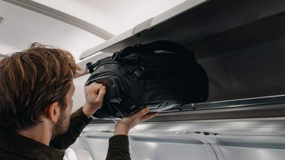 A man placing a Kit Bag 30L in the overhead locker on an airplane